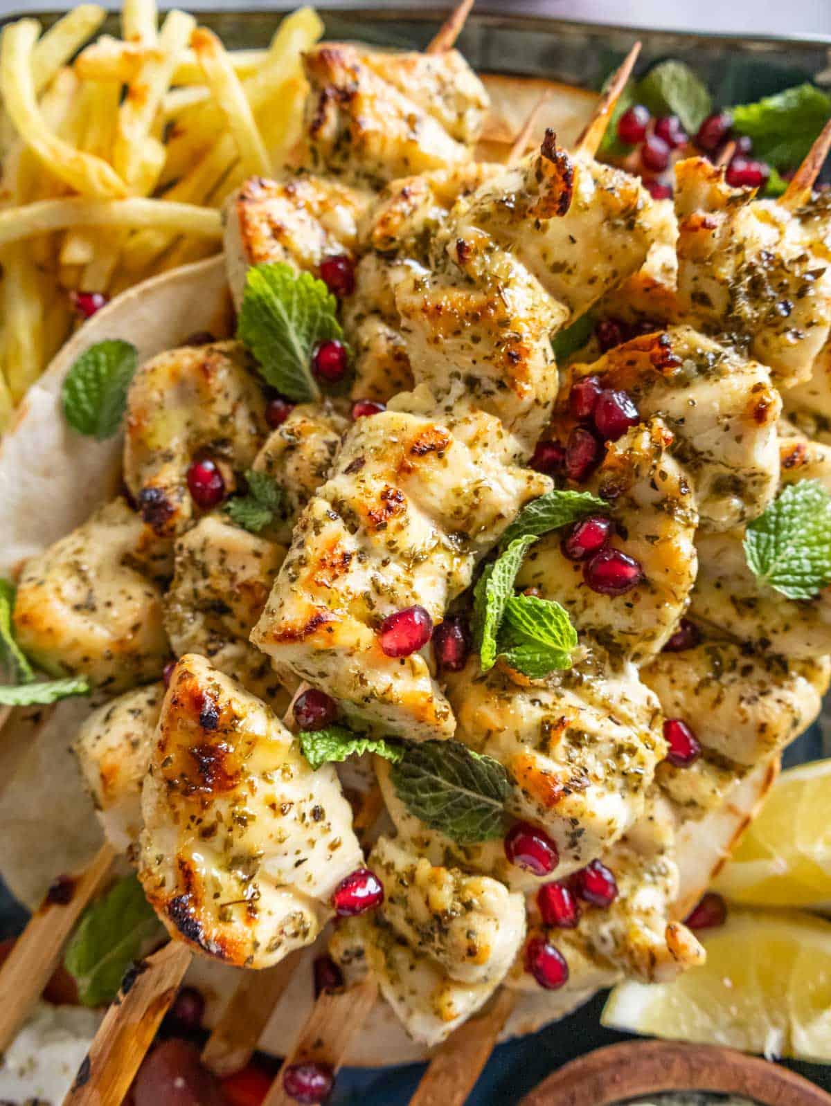 close-up shot of chicken souvlaki skewers on a plate, garnished with lemon and oregano