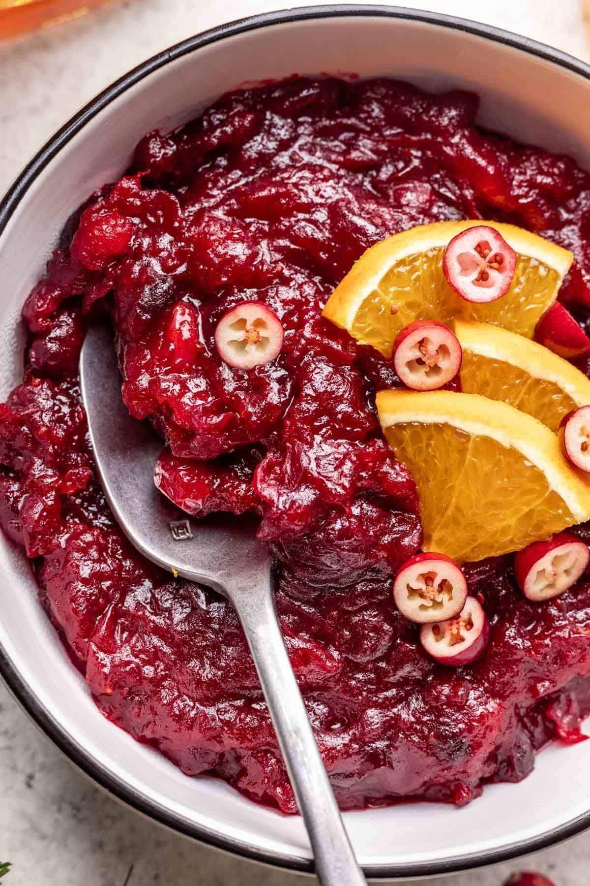 Close-up shot of a creamy cranberry sauce dip with orange zest garnished with fresh cranberries and orange slices