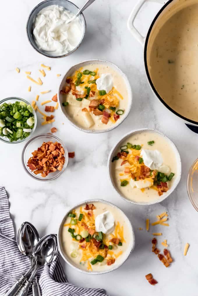 overhead shot of bowls of loaded baked potato soup with various toppings displayed