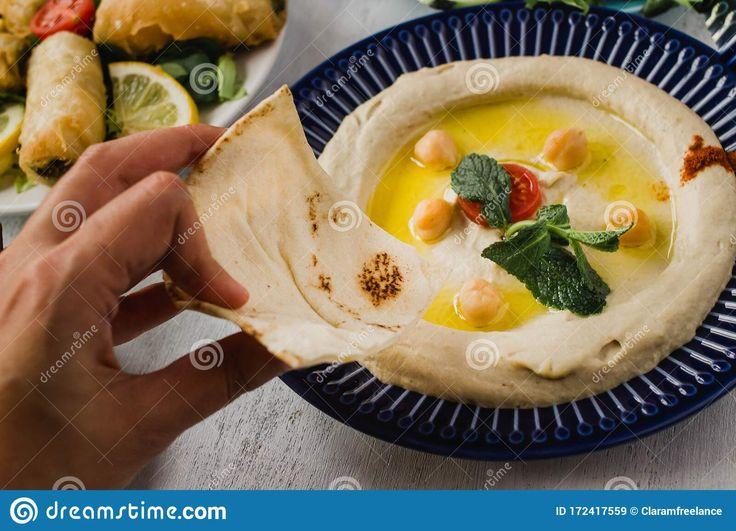 Close-up of a hand reaching for a piece of pita bread and hummus on a Mediterranean board
