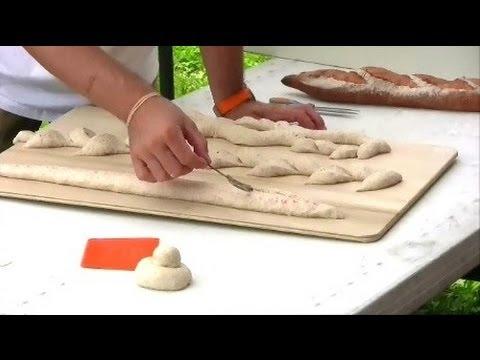 hands scoring a baguette dough with a lame