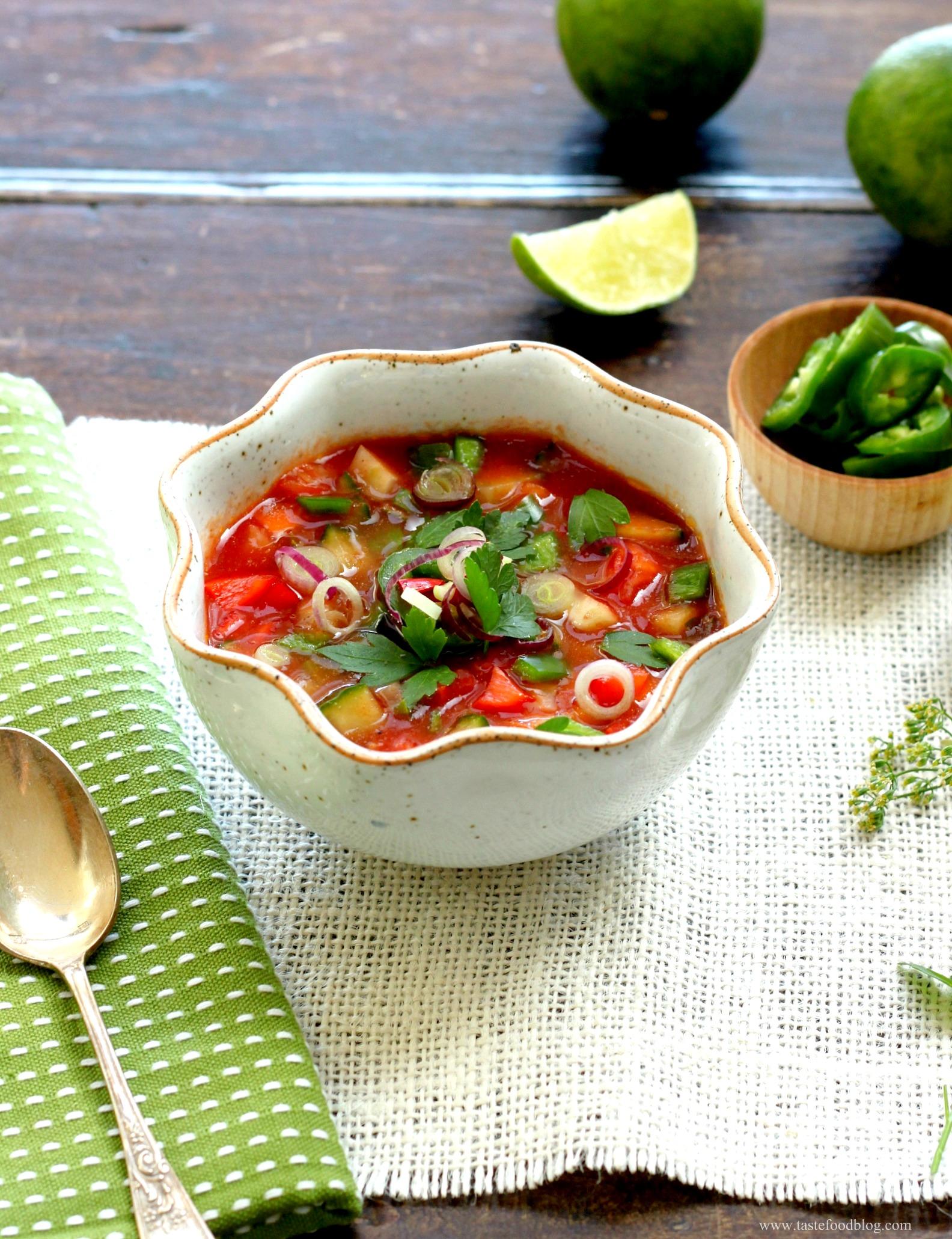 A bowl of spicy gazpacho garnished with fresh cilantro and lime wedges