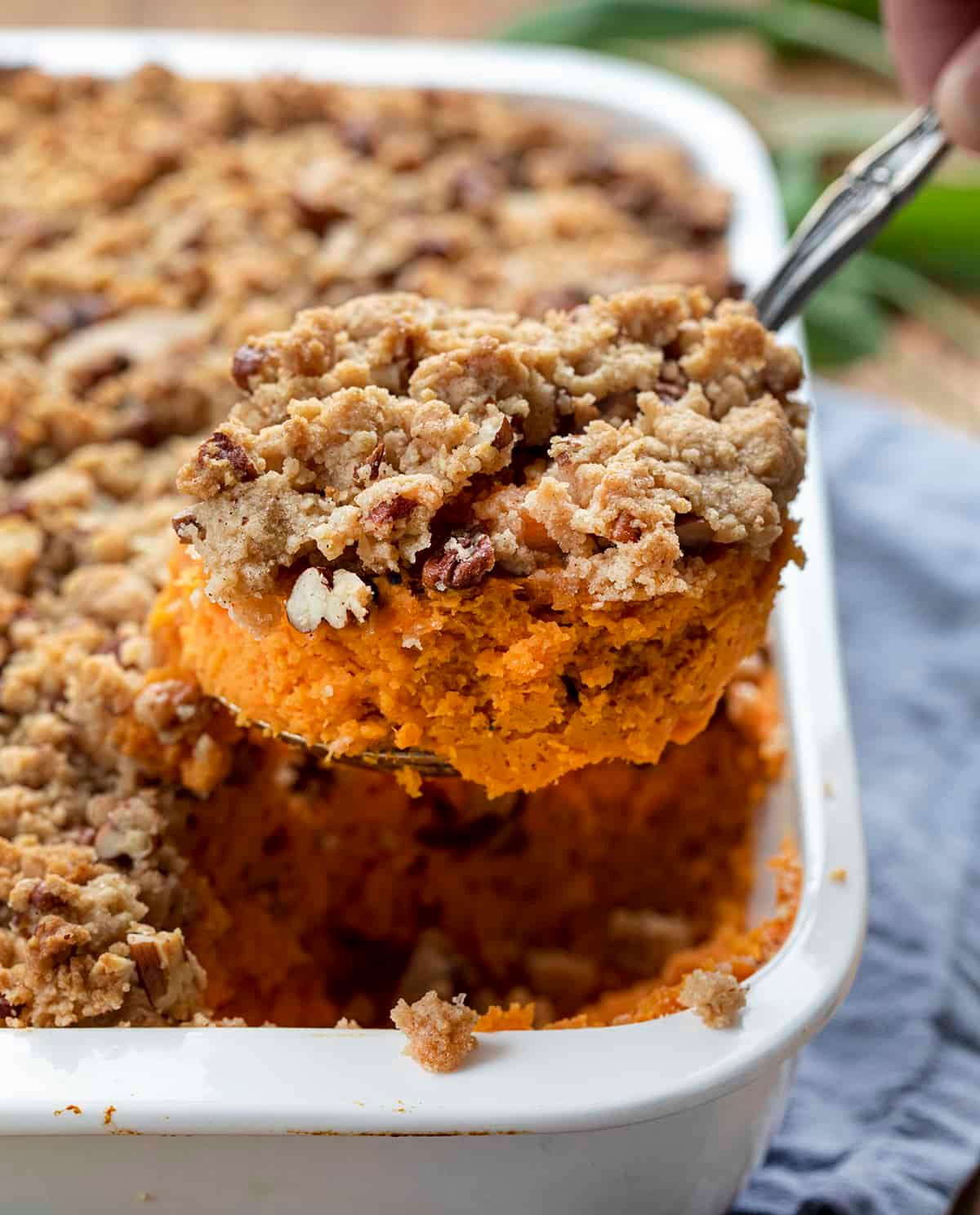 Hand sprinkling pecan streusel over sweet potato mixture in a baking dish.