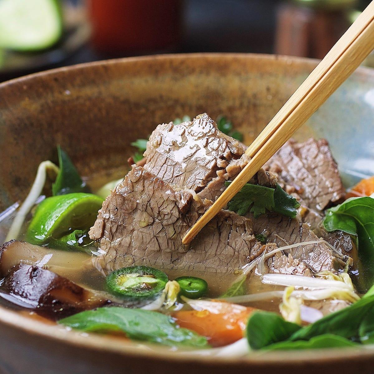 bowl of smoked brisket pho ga with fresh herbs and lime