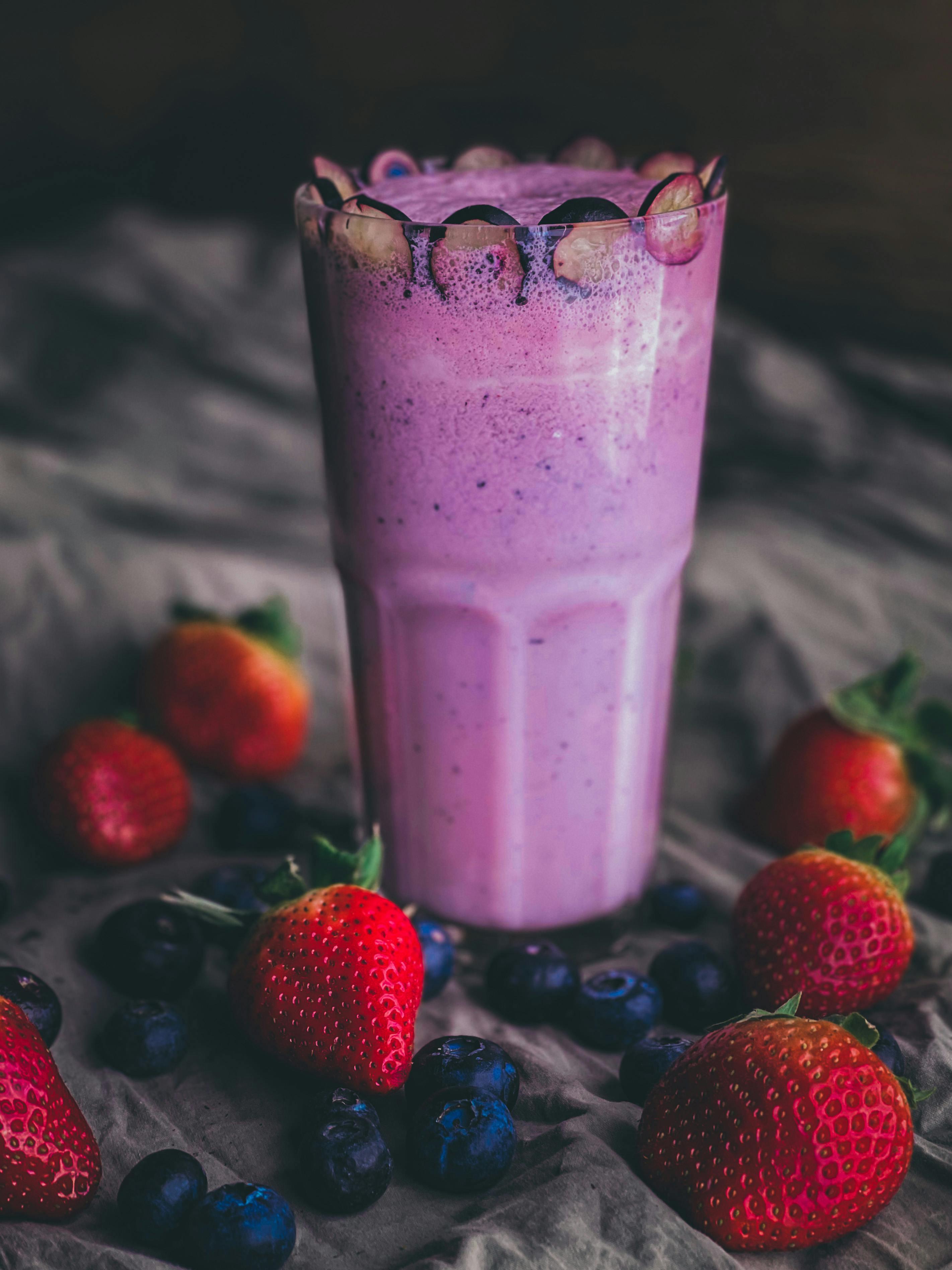 close up shot of a vibrant berry smoothie in a glass with berries and a spice shaker nearby