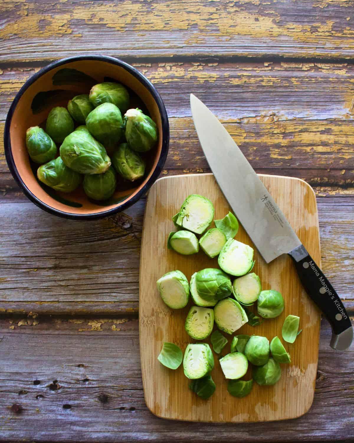 A close-up shot of fresh, vibrant green Brussels sprouts, some whole, some halved, scattered on a rustic wooden cutting board next to a chef's knife and a small bowl of olive oil