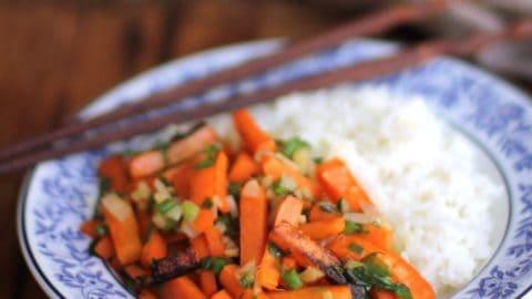 a person serving a bowl of Carrot Craze Vegetable Stir-Fry over rice, with a happy expression
