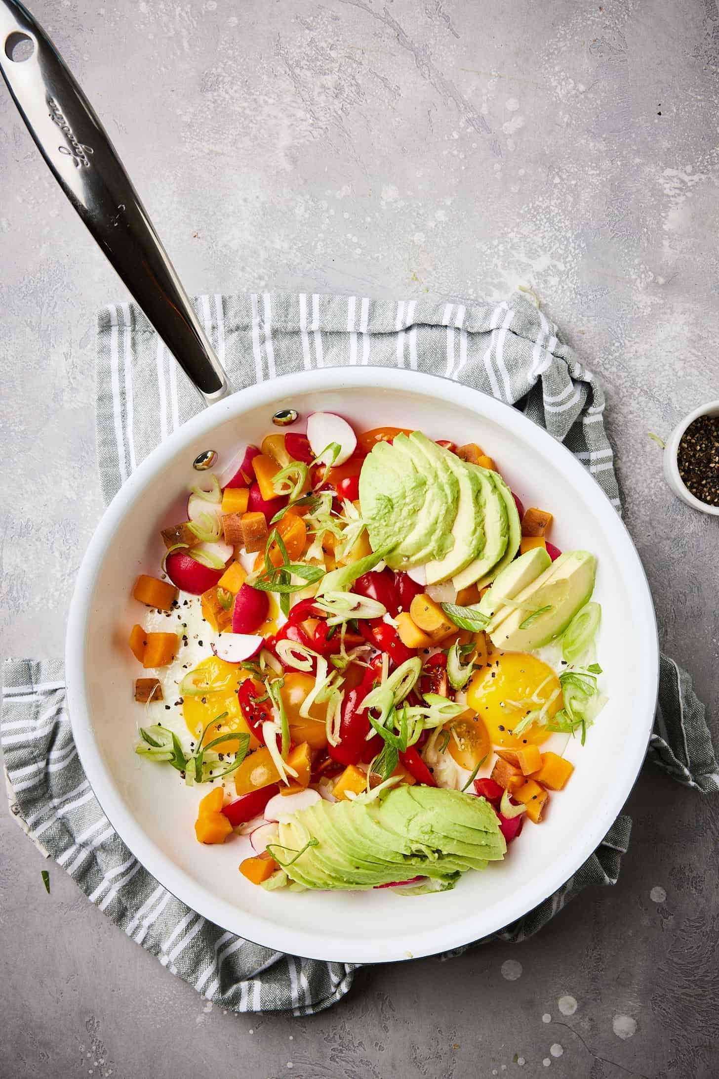 a person adding diced avocado to a vibrant paleo bowl