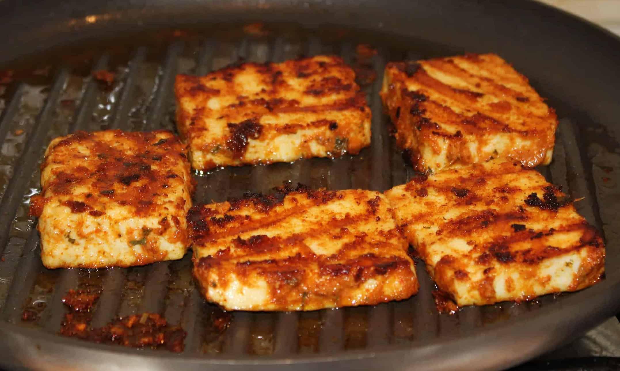 Close-up shot of flavorful paneer tikka cubes with a sprinkle of cinnamon on a grill pan