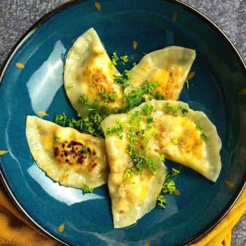 Overhead shot of several jollof pierogi arranged on a rustic wooden board, garnished with fresh herbs