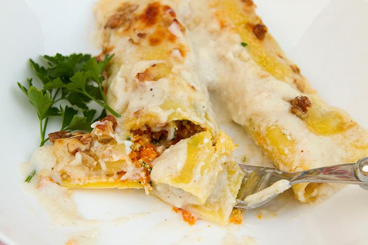 Close-up of a baked butternut squash and ricotta cannelloni dish with melted cheese and herbs