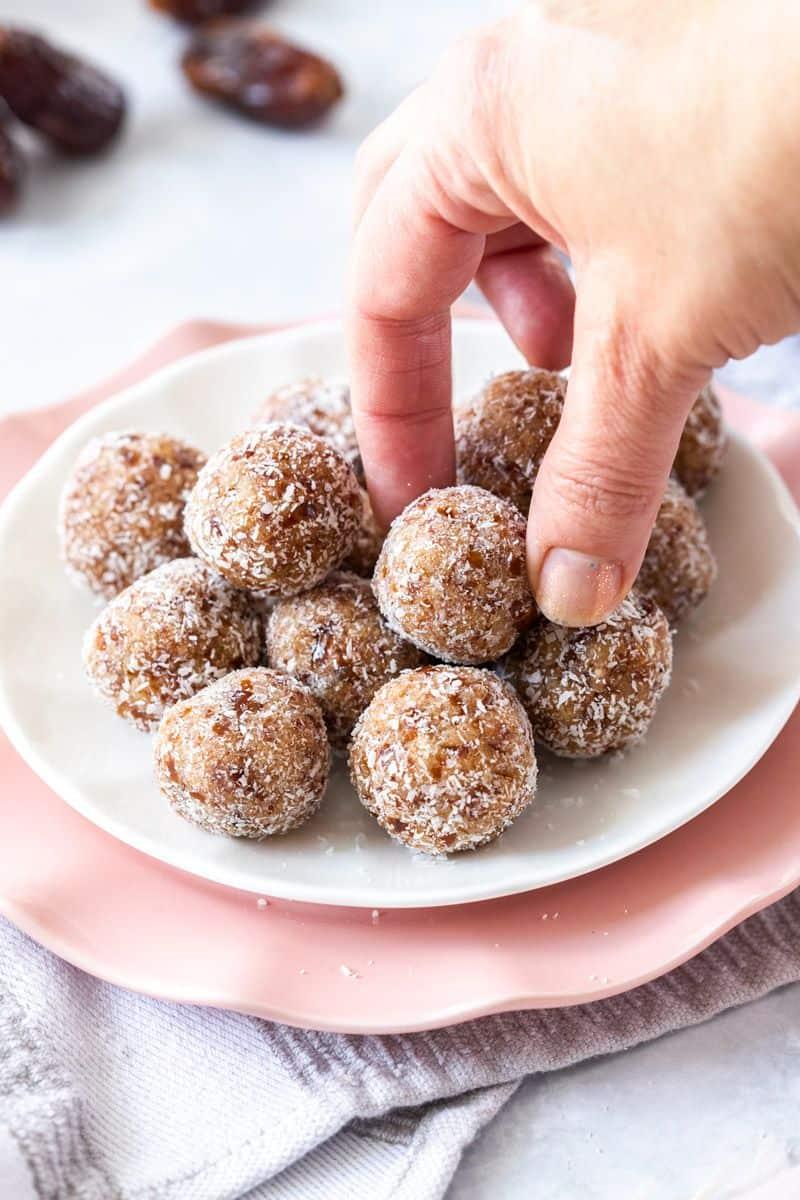 a child reaching for a coconut almond bliss ball on a plate