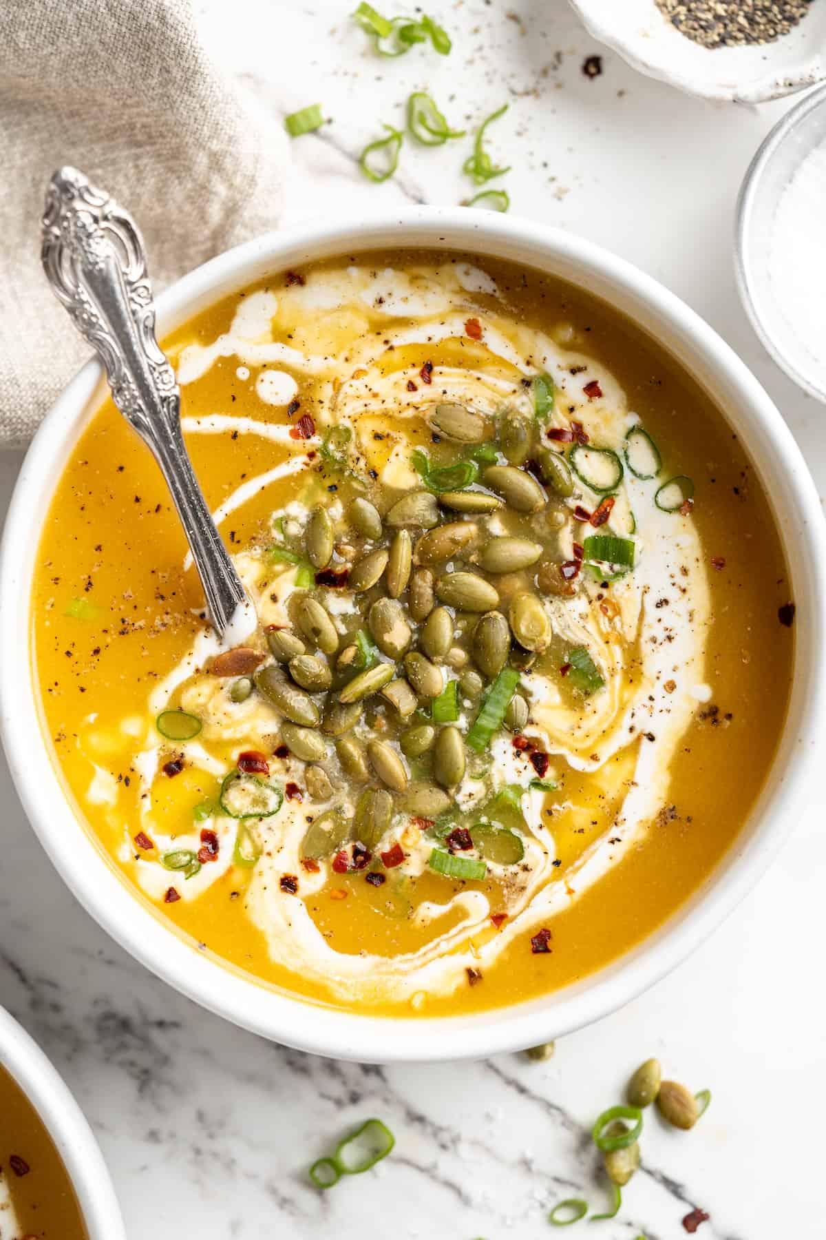 bowl of vegan roasted garlic pumpkin soup garnished with coconut cream and herbs