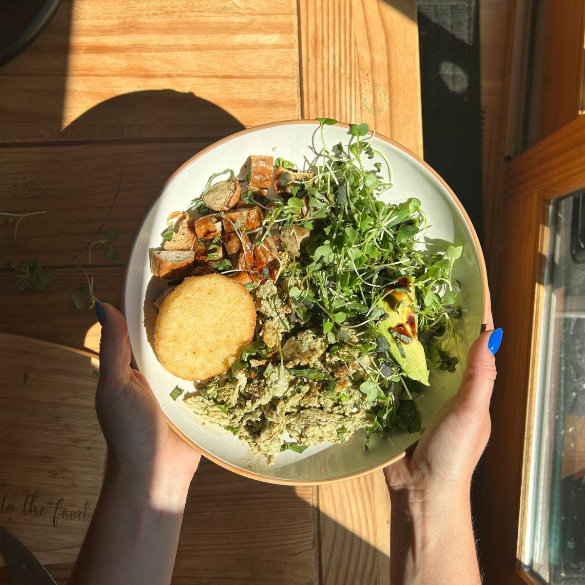 Hands holding a healthy basil veggie bowl, sunlit kitchen background