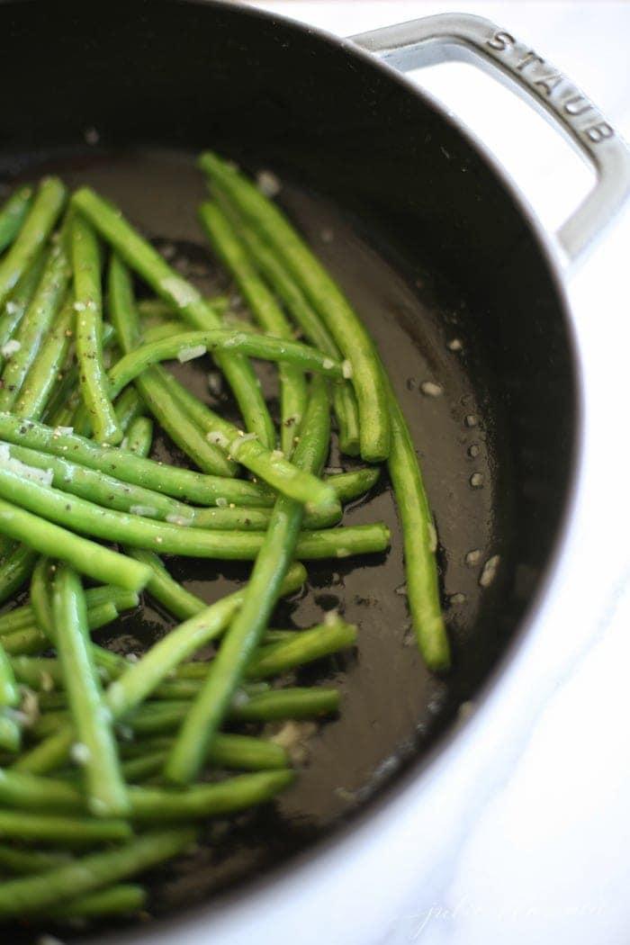 Close-up of green beans braising in butter with shallots in a cast iron skillet
