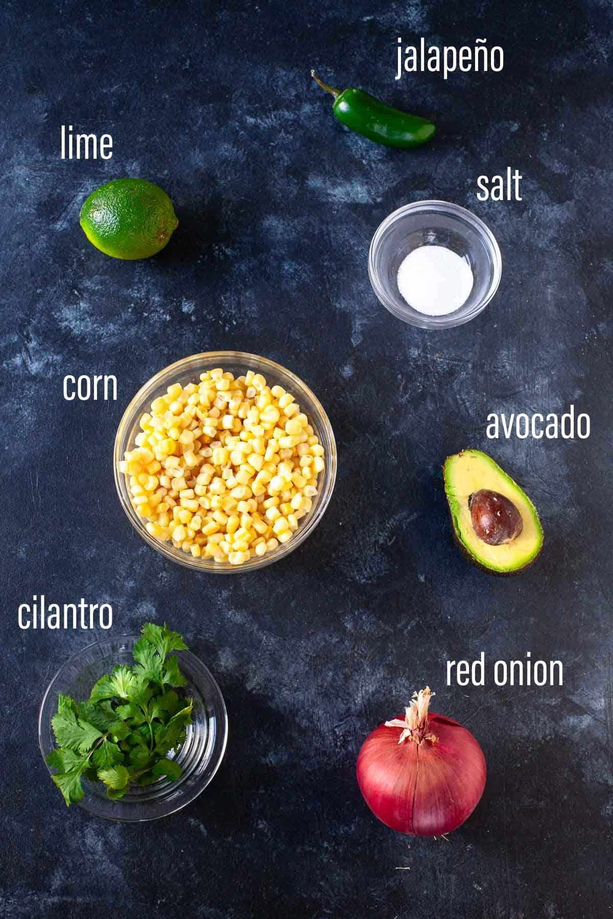 ingredients for corn and avocado salsa laid out on a wooden table