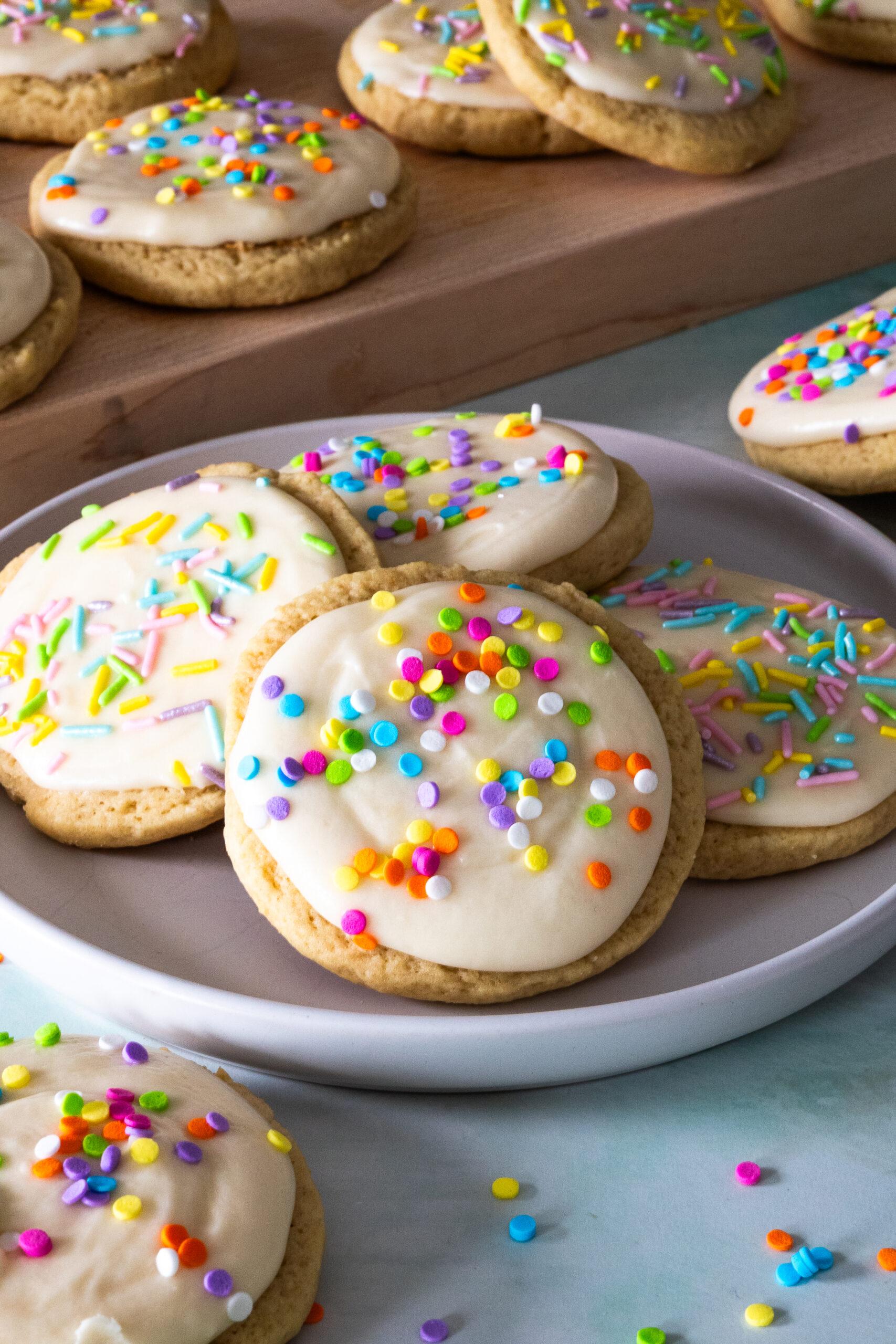 Close-up of freshly baked sprinkle sugar cookies with smooth, colorful icing on a cooling rack