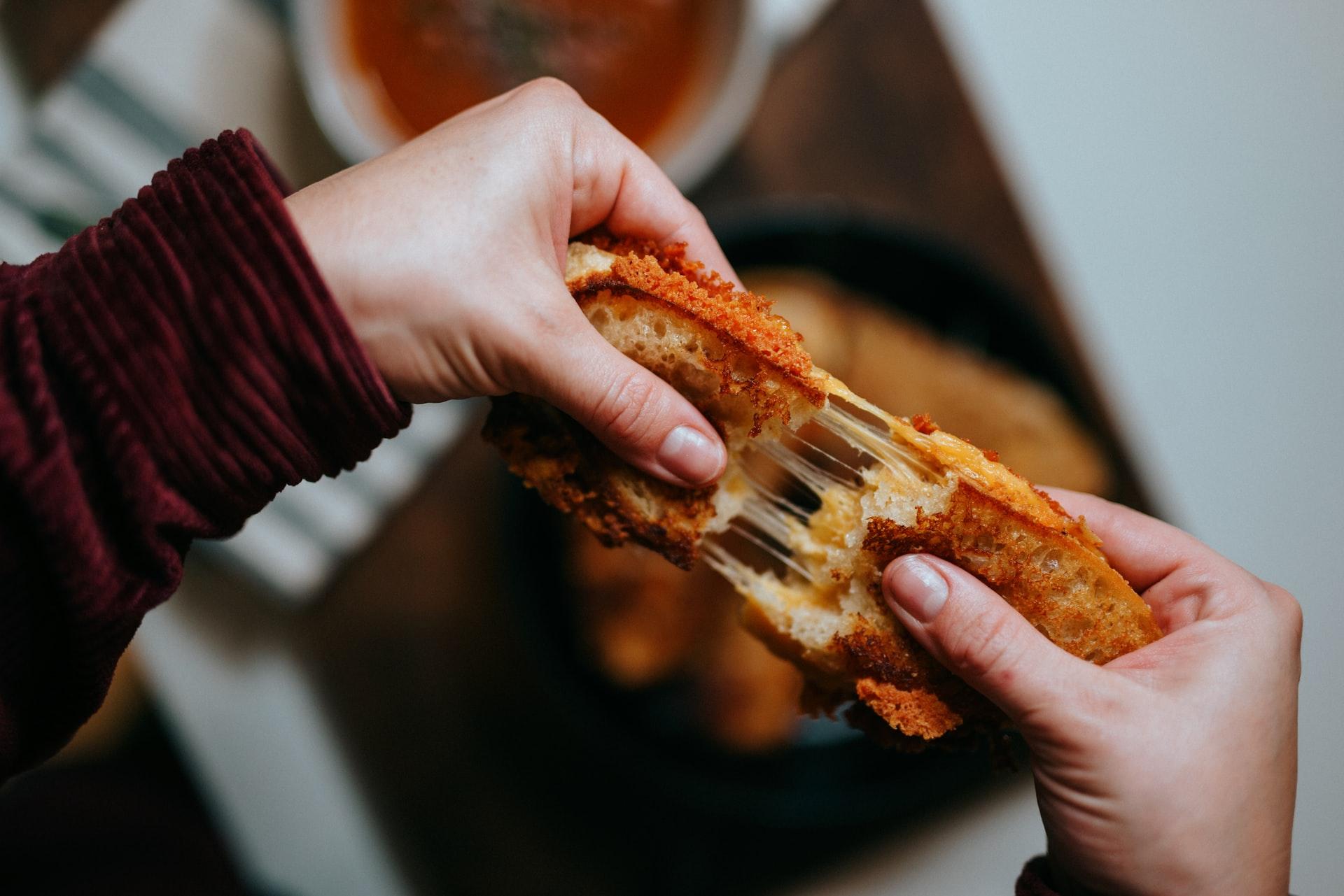 person happily biting into a pizza grilled cheese sandwich, steam rising, cozy kitchen background