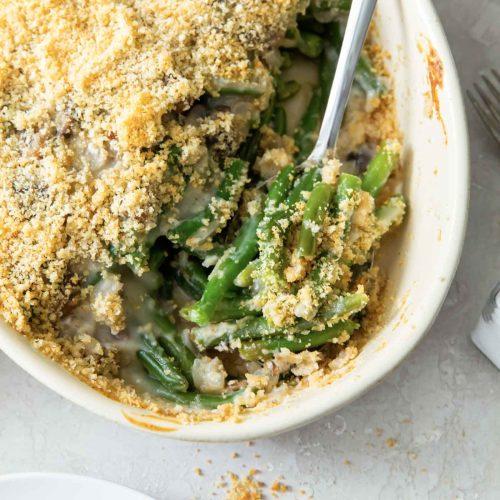 A person sprinkling fresh herbs over the crumb topping of an unbaked green bean casserole.