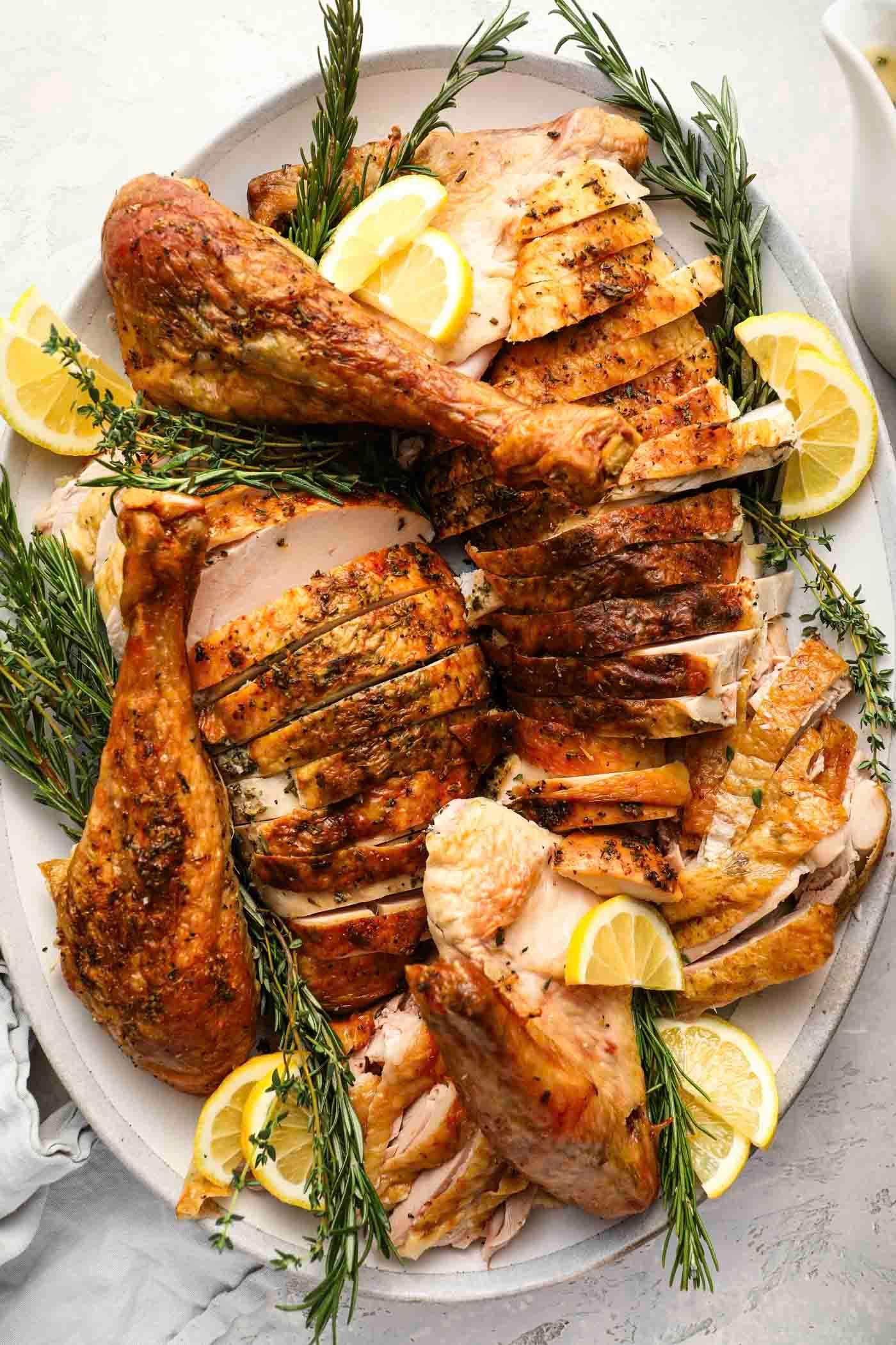 carved roasted turkey slices on a serving platter with fresh herbs