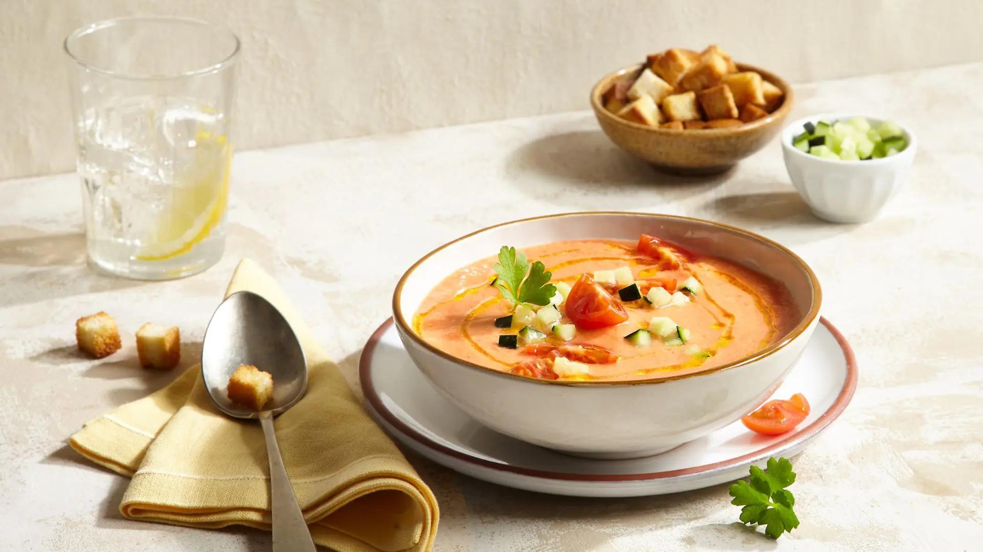 A table setting with a bowl of gazpacho and some crusty bread