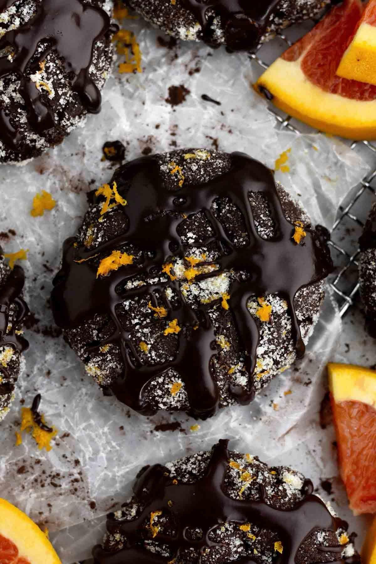 A hand dipping a chocolate cookie into a vibrant orange glaze