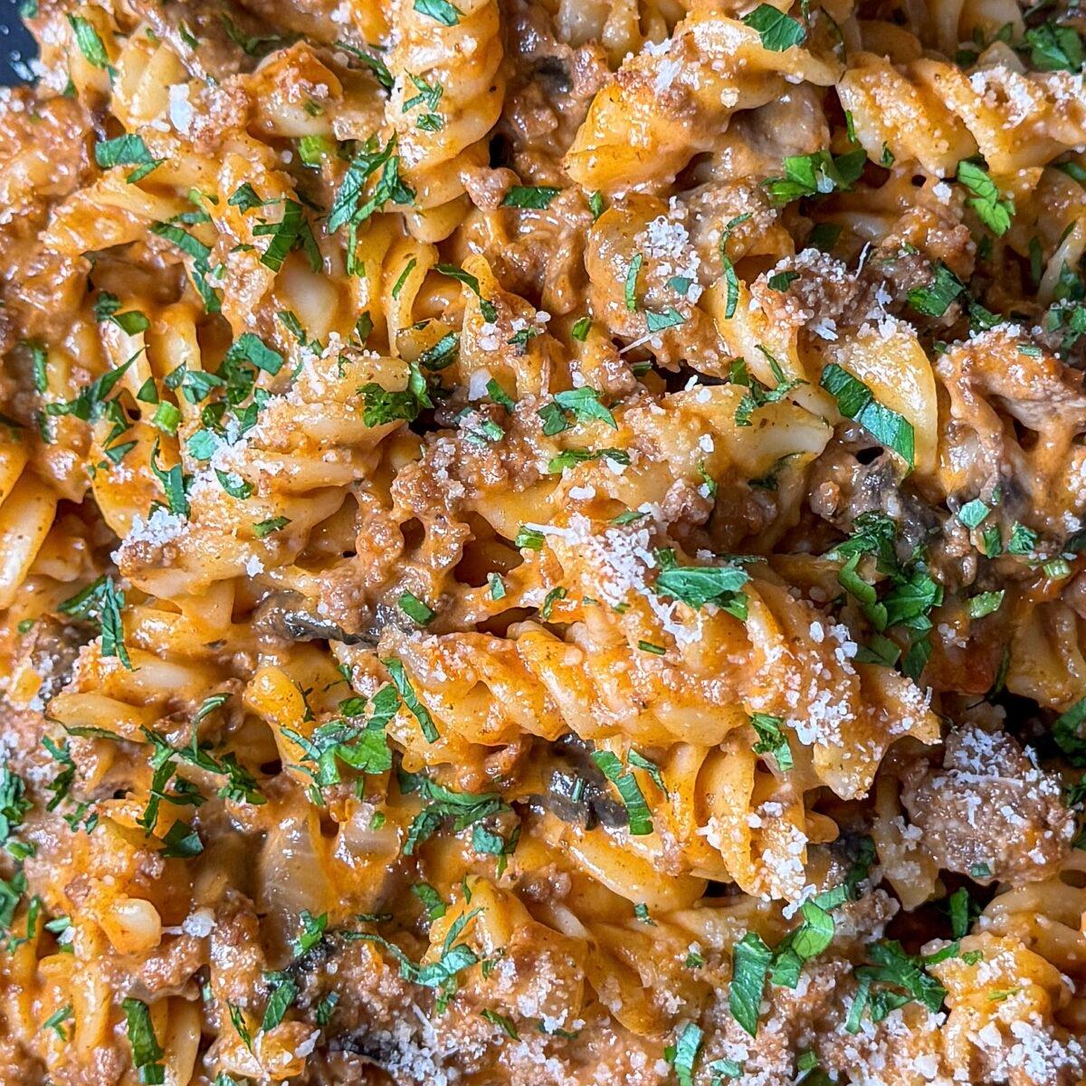 close-up of ground beef simmering in a tomato-cream sauce with pasta