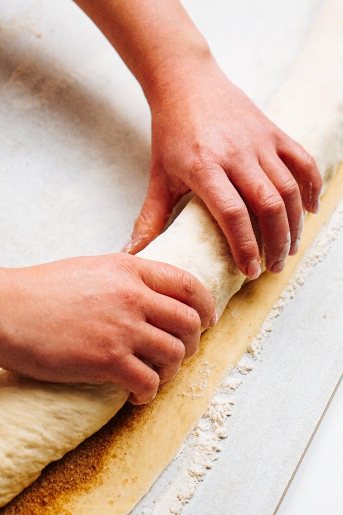 close up shot of cinnamon roll dough being kneaded on a floured surface