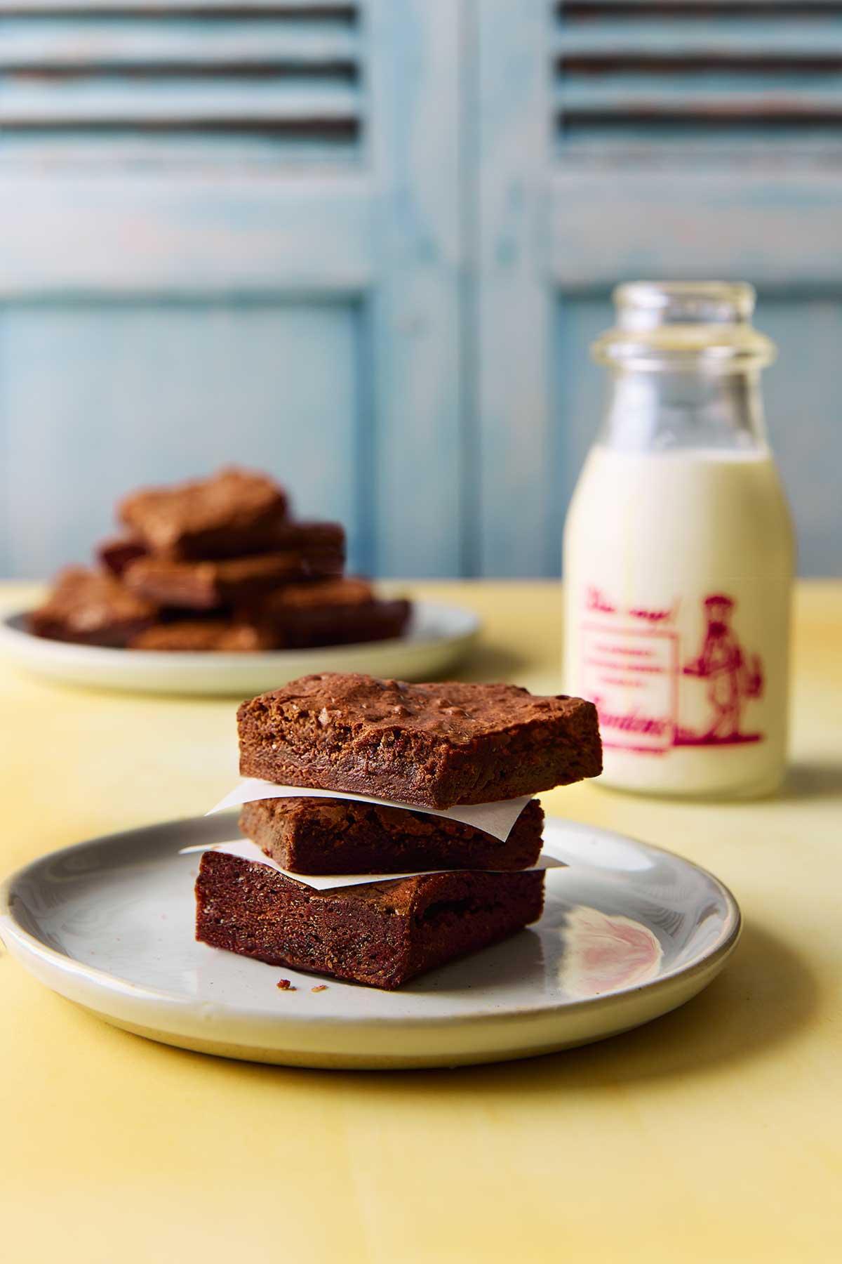 A close up shot of brownies on the counter with a glass of milk