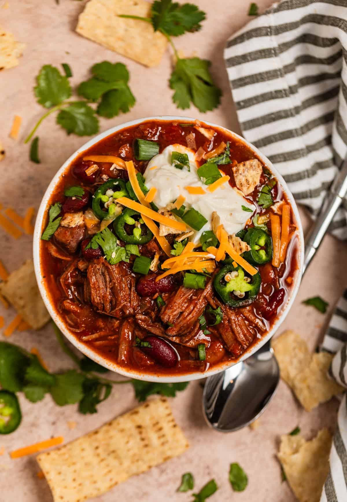 Close-up of a slow-cooked chili-pepper beef roast, fork-tender, garnished with fresh cilantro and sliced red chilies, rich sauce, rustic setting.
