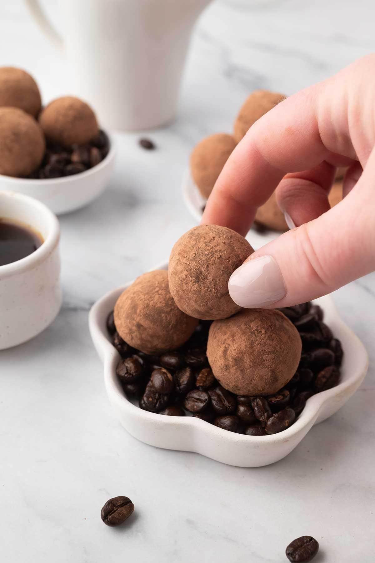 Close-up of a perfectly rolled and cocoa-dusted espresso truffle on a white plate.