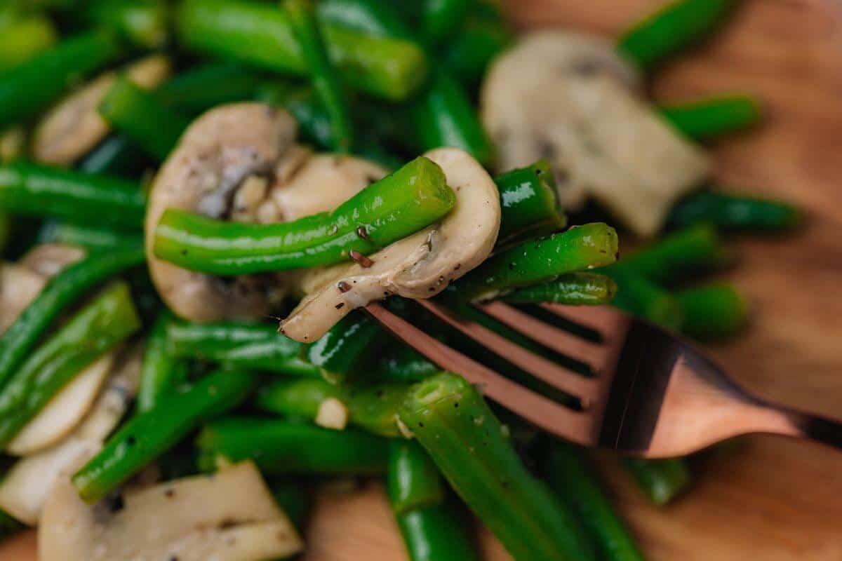 Close-up of fresh green beans and sliced cremini mushrooms on a cutting board