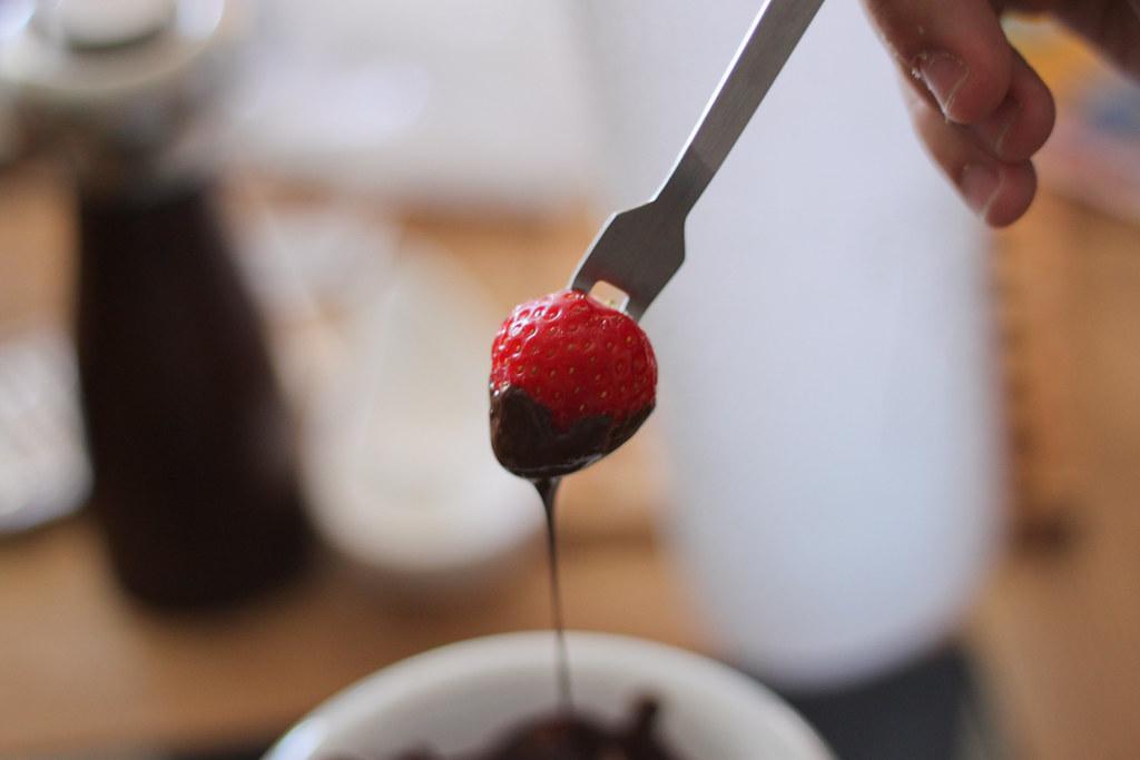 Someone dipping a strawberry into Thai Coconut Curry Chocolate Fondue, close-up