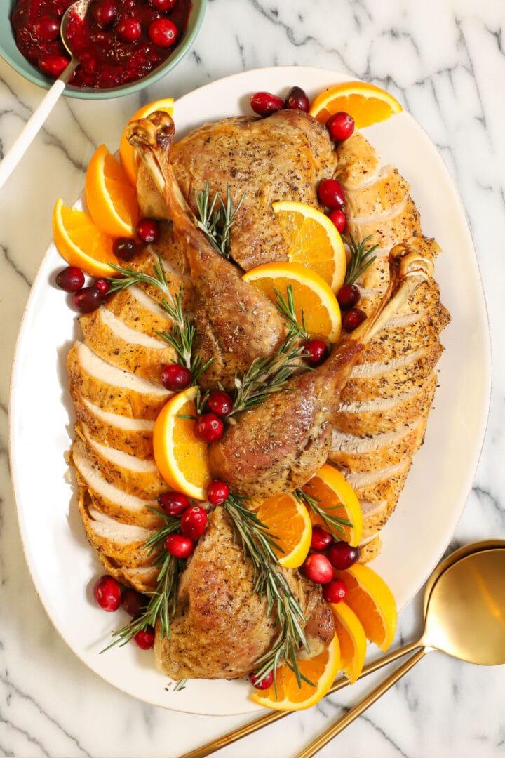 beautifully carved oven roasted turkey on a large platter surrounded by fresh rosemary, oranges, and cranberries, holiday setting