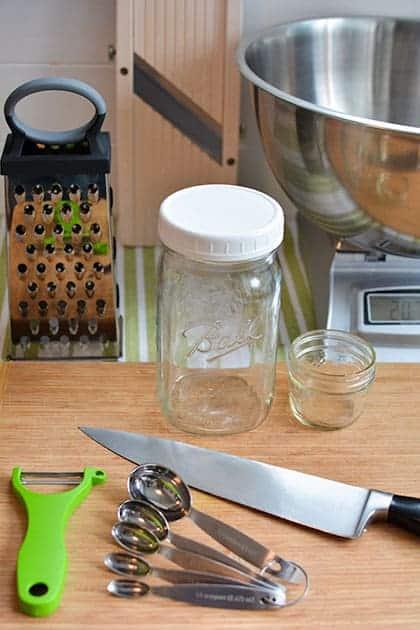 A sunlit kitchen counter showing a jar of sauerkraut-infused oil next to a rustic wooden cutting board