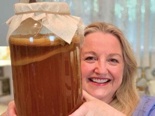 a person happily holding a glass jar of homemade kombucha