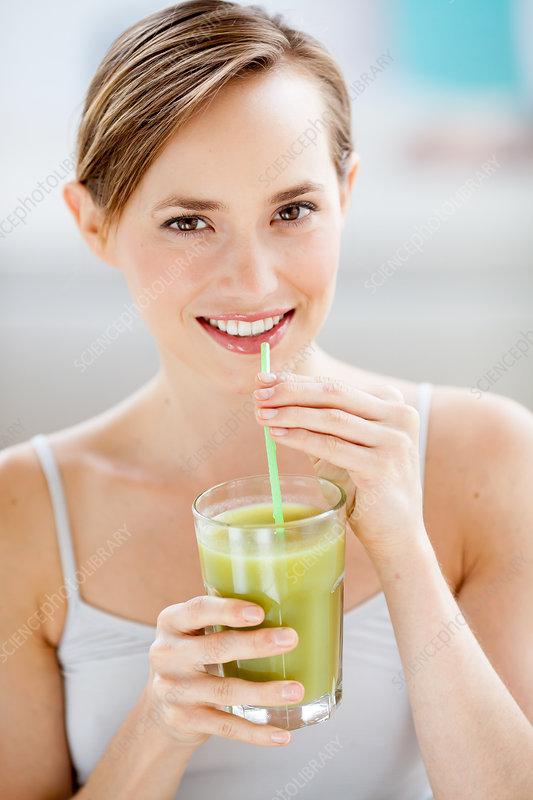 close-up shot of a person smiling while holding a glass of green smoothie with a straw, berries in the background