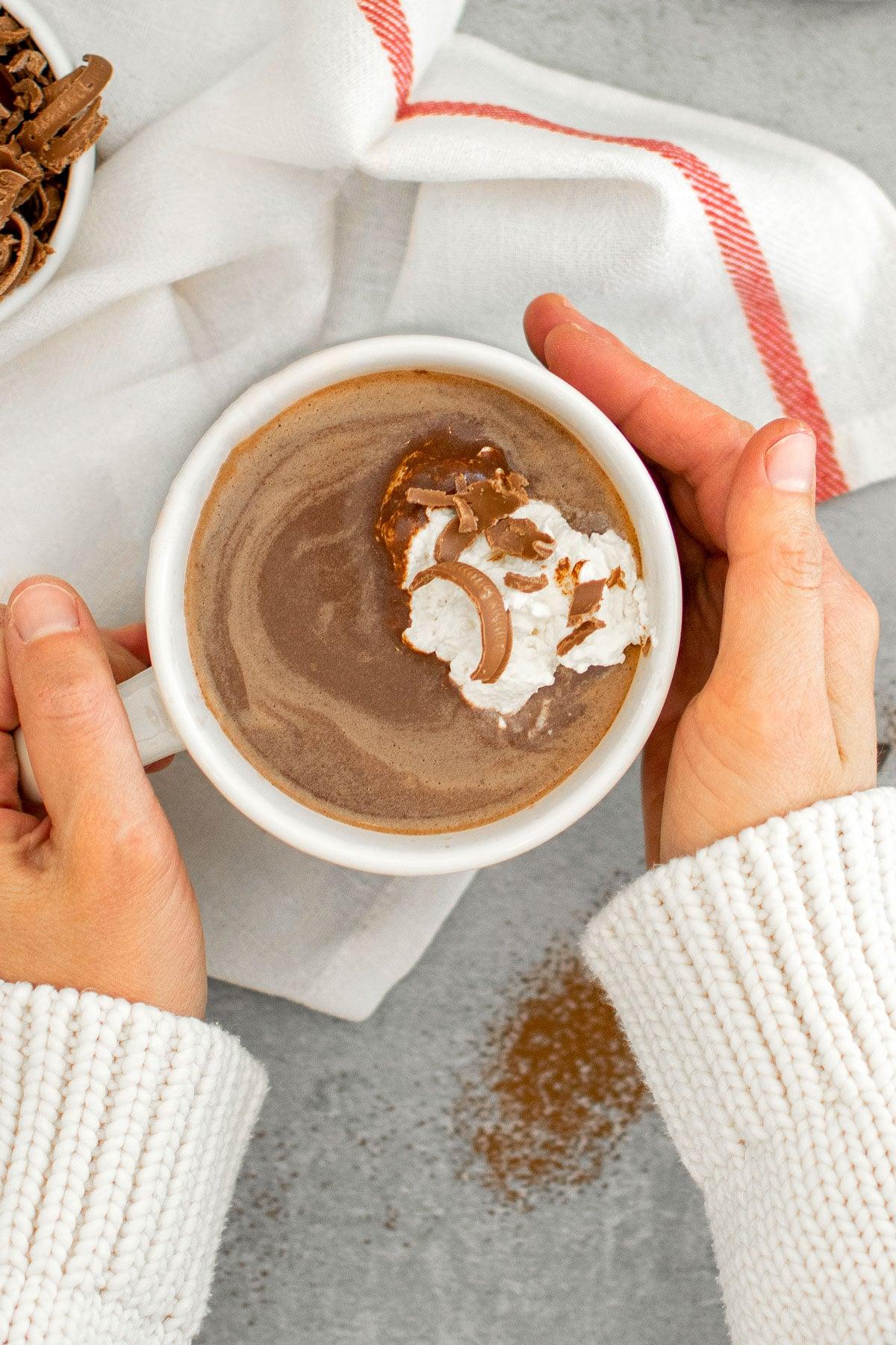 close-up of a hand gently swirling a generous dollop of fresh homemade whipped cream into a steaming mug of creamy hot chocolate