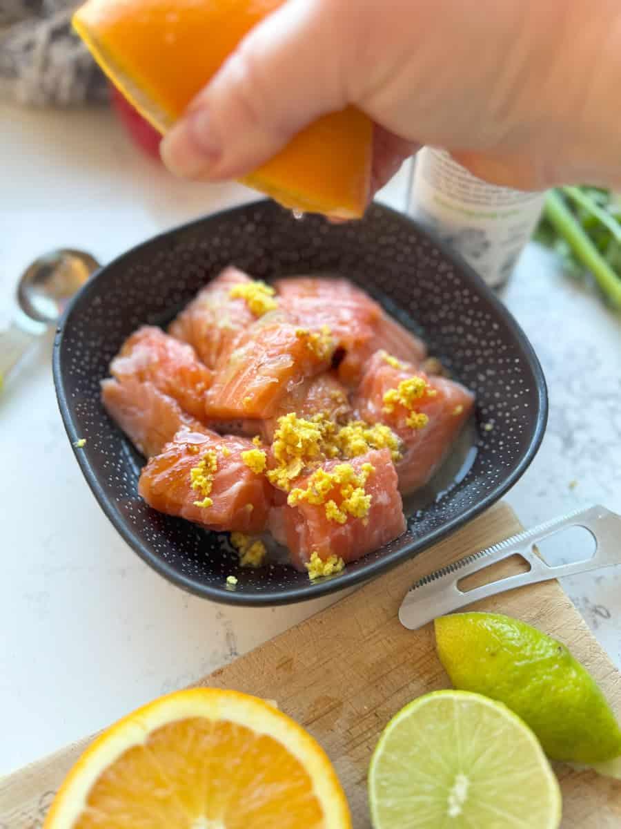 close up of raw salmon cubes marinating in a bowl with dill and lemon slices