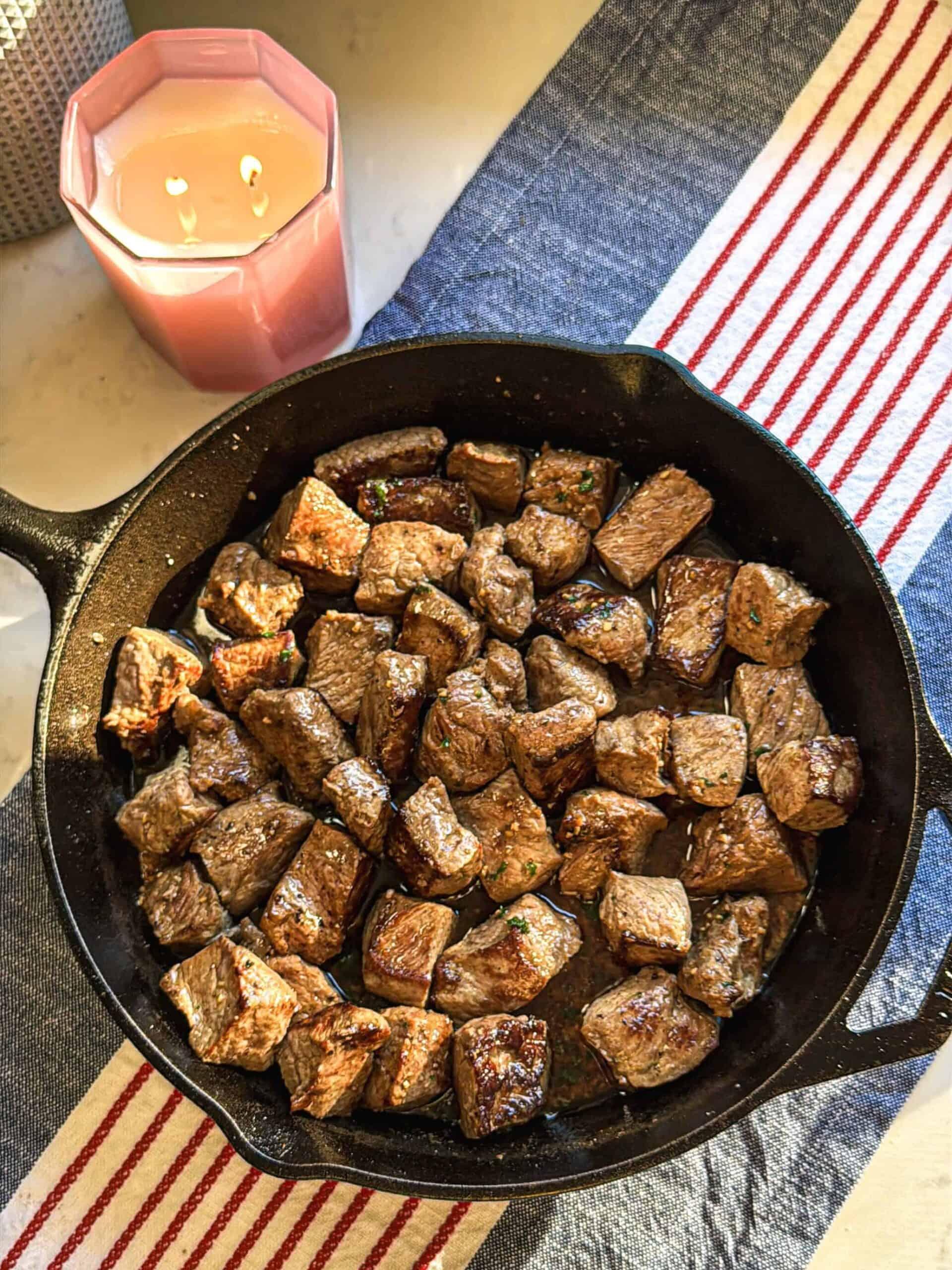 overhead shot of chili-roasted beef cubes in a cast iron skillet with fresh herbs