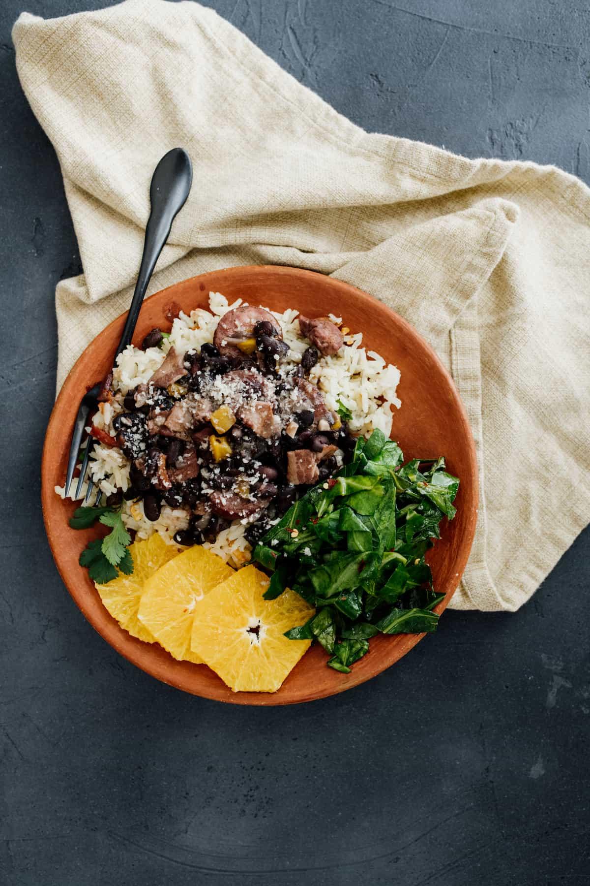 Authentic Brazilian feijoada served in a rustic bowl with rice, collard greens, and orange slices