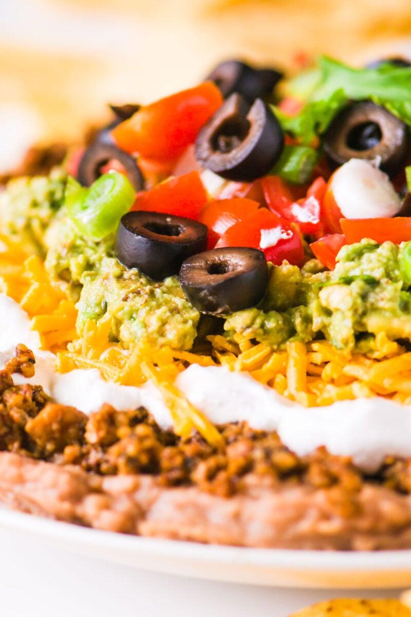 Close-up shot of a seven layer dip with baked tortilla chips and various toppings.