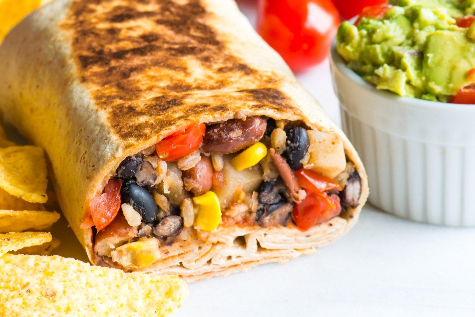 a close-up shot of a burrito shawarma cut in half, revealing the layers of rice, beans, and seasoned meat