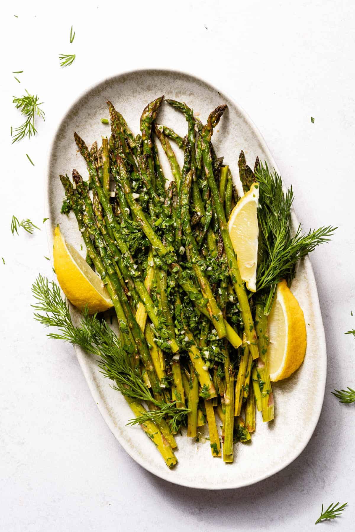 Overhead shot of a plate of grilled asparagus with lemon wedges and fresh herbs