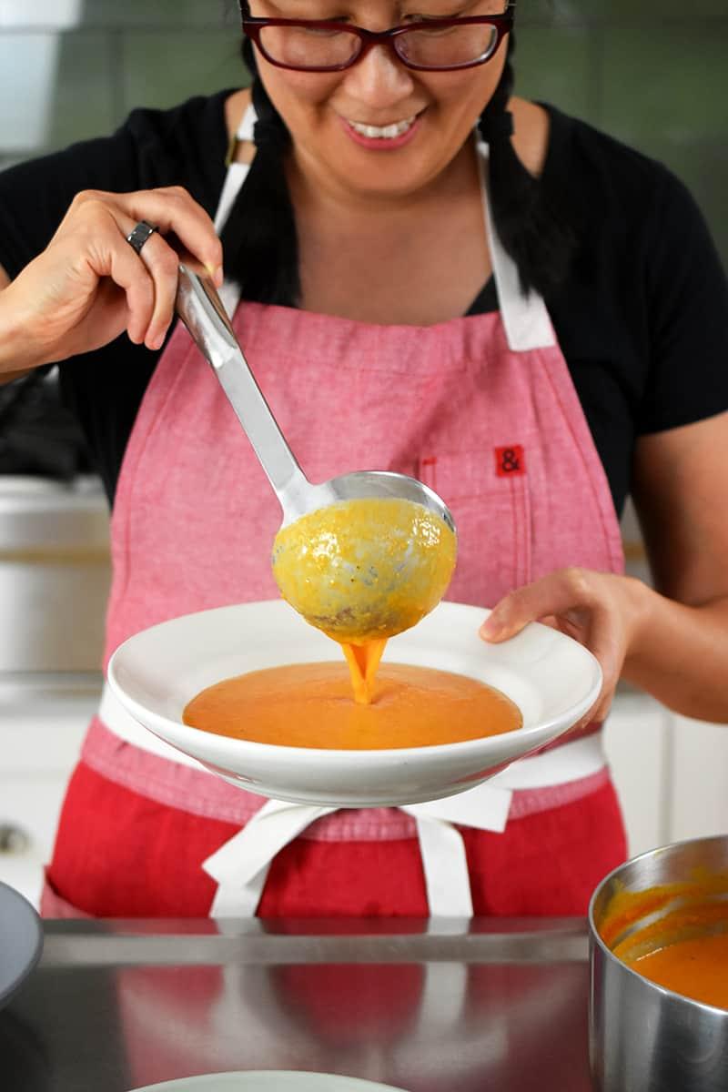 woman smiling while preparing tomato soup