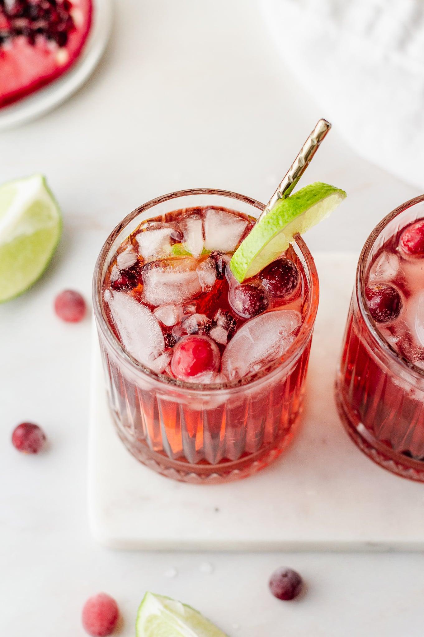 overhead shot of ingredients for pomegranate mocktail: pomegranates, limes, sparkling water, cranberries on a wooden board
