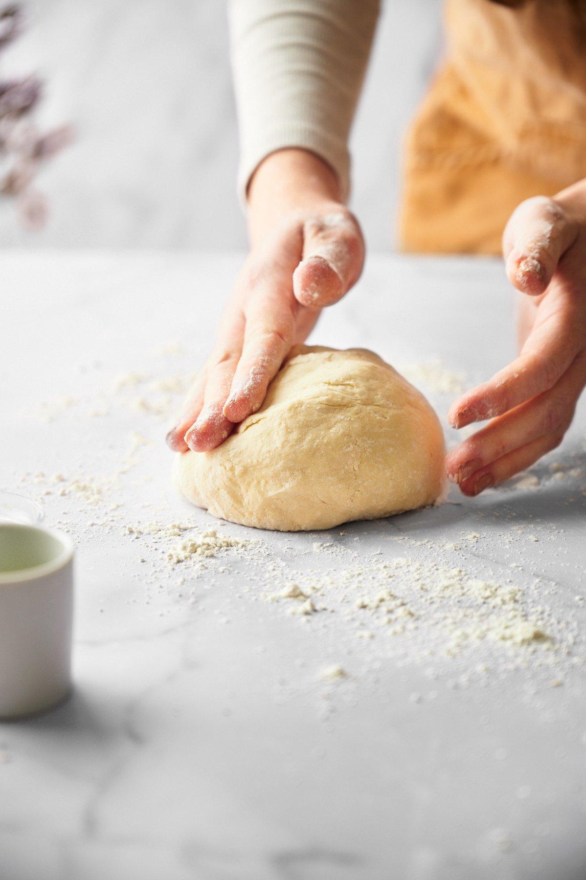 woman kneading wheat flour pizza dough on a floured surface