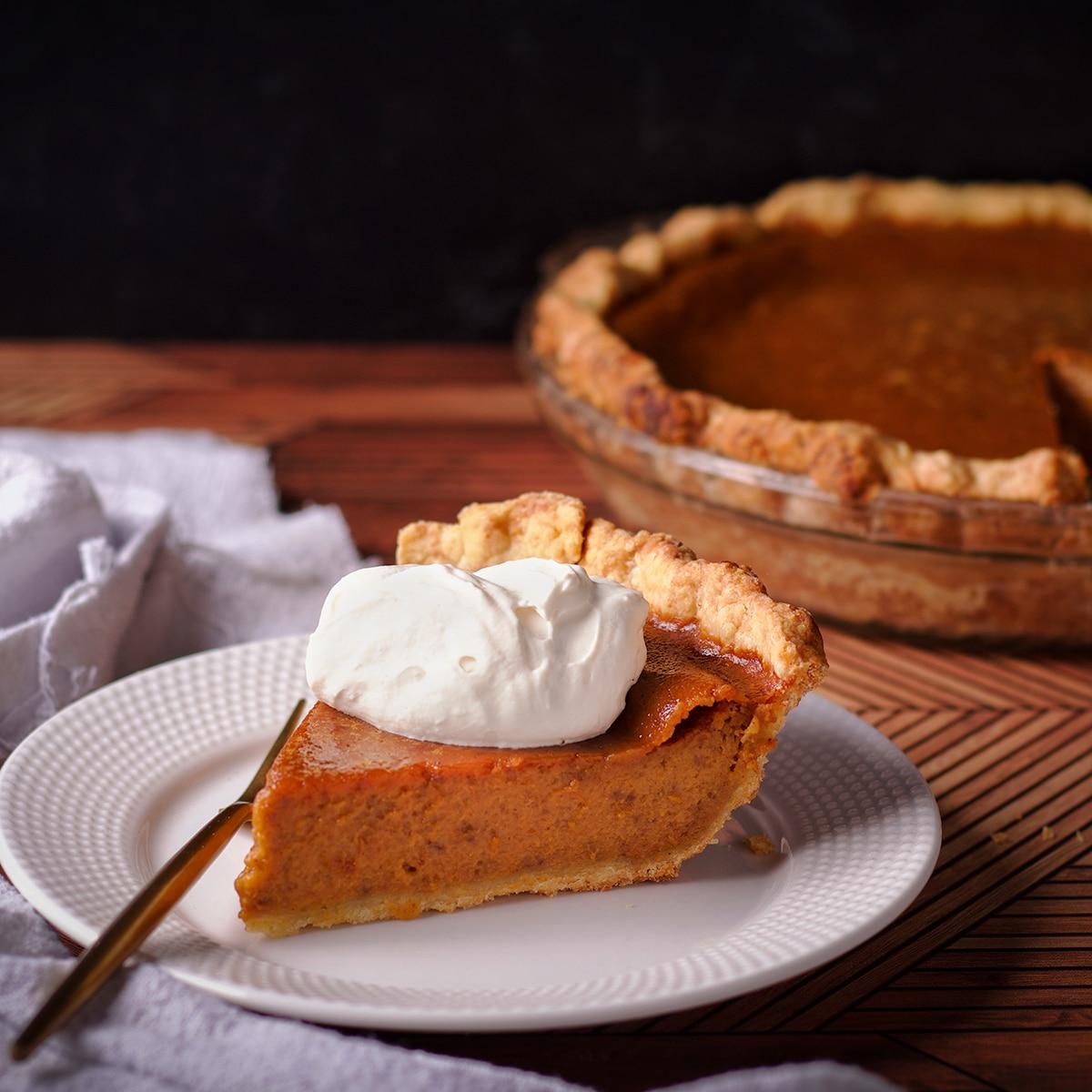 Rustic maple pumpkin pie with whipped cream and autumn leaves, close-up, warm lighting