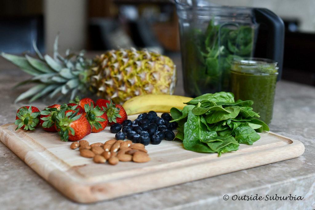 a close-up shot of the ingredients for the acai berry green smoothie: acai berries, spinach, banana, and almond milk, arranged artfully on a wooden countertop