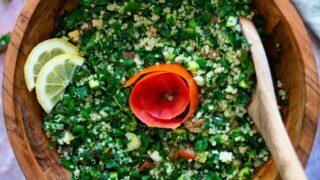 Close-up shot of a hand placing a spoonful of Tabbouleh into a tomato half.